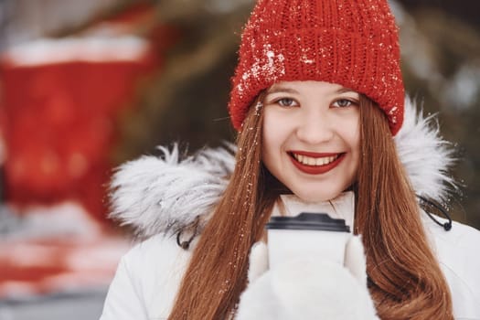 With cup of drink in hands. Happy young woman standing outdoors and celebrating christmas holidays.