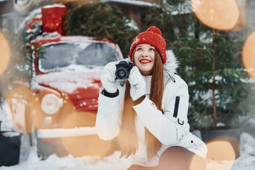 With camera in hands. Happy young woman standing outdoors and celebrating christmas holidays.