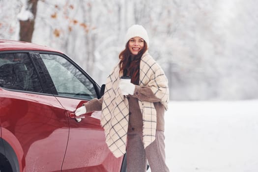 Cheerful emotions. Beautiful young woman is outdoors near her red automobile at winter time.