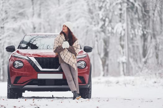 In front of her car. Beautiful young woman is outdoors near her red automobile at winter time.