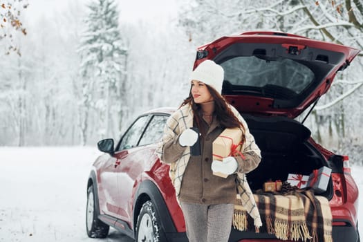 Sitting on the back of a car. Beautiful young woman is outdoors near her red automobile at winter time.