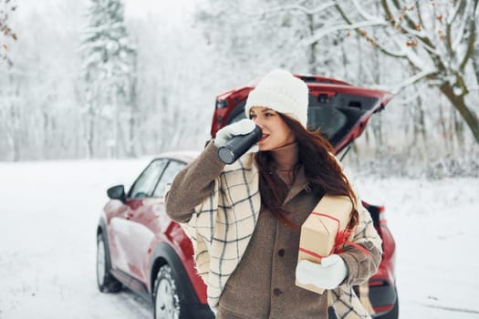 In front of her car. Beautiful young woman is outdoors near her red automobile at winter time.