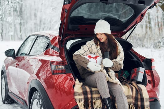 Holiday presents. Beautiful young woman is outdoors near her red automobile at winter time.