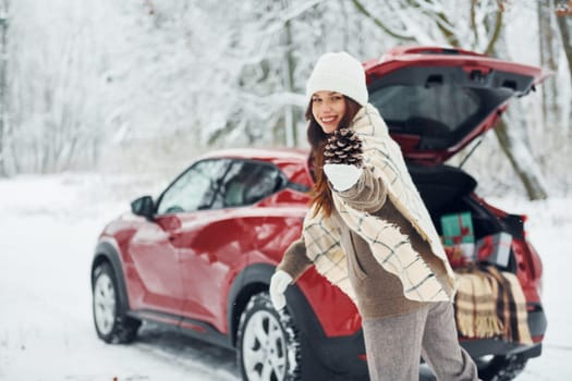 In the forest. Beautiful young woman is outdoors near her red automobile at winter time.