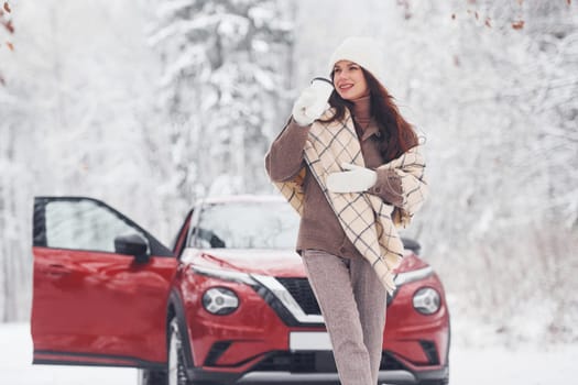 Cheerful emotions. Beautiful young woman is outdoors near her red automobile at winter time.