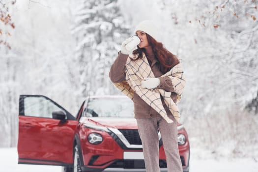 Cheerful emotions. Beautiful young woman is outdoors near her red automobile at winter time.