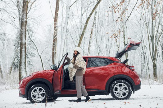 Opening the door. Beautiful young woman is outdoors near her red automobile at winter time.