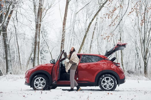 Opening the door. Beautiful young woman is outdoors near her red automobile at winter time.