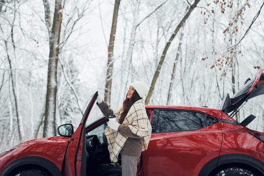 Opening the door. Beautiful young woman is outdoors near her red automobile at winter time.