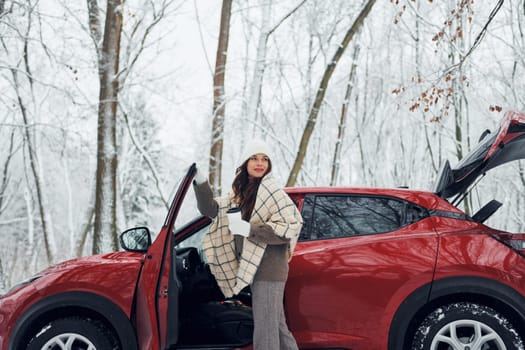 Opening the door. Beautiful young woman is outdoors near her red automobile at winter time.