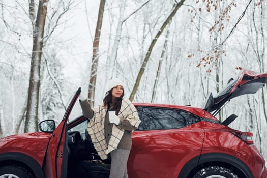 Opening the door. Beautiful young woman is outdoors near her red automobile at winter time.