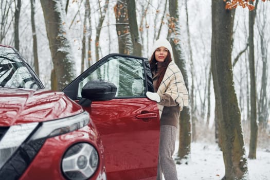 Positive emotions. Beautiful young woman is outdoors near her red automobile at winter time.