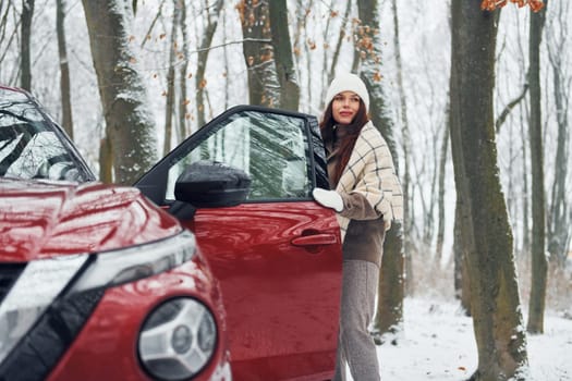 Positive emotions. Beautiful young woman is outdoors near her red automobile at winter time.