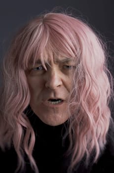 Portrait of an angry middle-aged man in a pink wig. Close-up. Vertical frame.