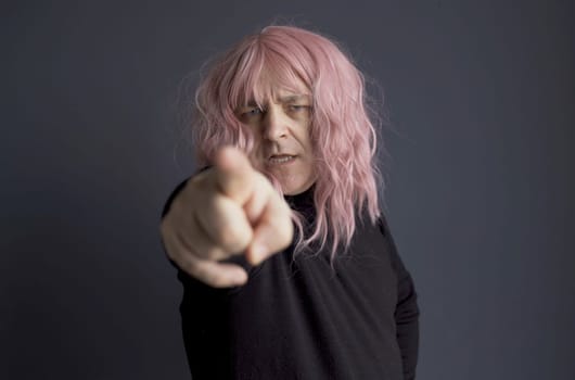 Portrait of a man in a pink wig, looking and pointing his finger at the camera. close-up.