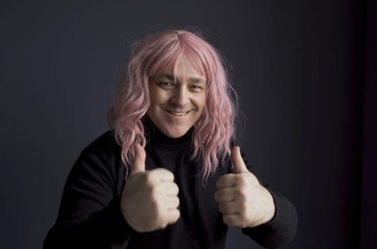 Positive man in a pink wig shows a gesture with his hands - thumbs up, great. Close-up.