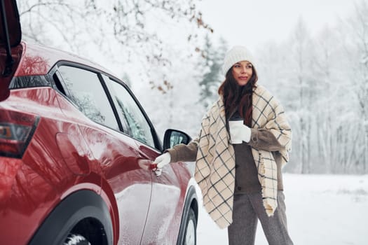 Positive emotions. Beautiful young woman is outdoors near her red automobile at winter time.