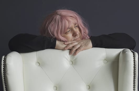 A portrait of a man in a pink wig, who is leaning on a white armchair, looks away. close-up.