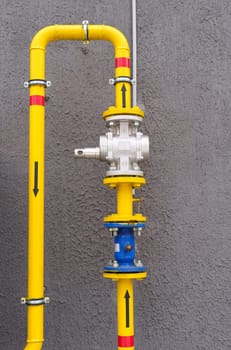 Yellow gas pipe with a shut-off - turn-on valve, connected to the wall of the building. Vertical frame.