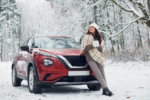Beautiful winter background. Beautiful young woman is outdoors near her red automobile at winter time.