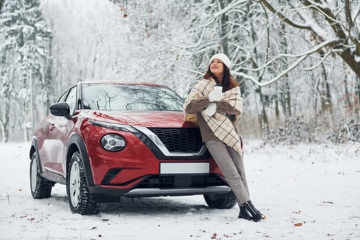 Beautiful winter background. Beautiful young woman is outdoors near her red automobile at winter time.