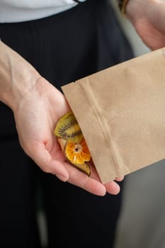 In the hands of a woman is a paper bag with candied fruits. Close-up.