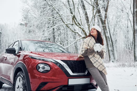 Beautiful winter background. Beautiful young woman is outdoors near her red automobile at winter time.