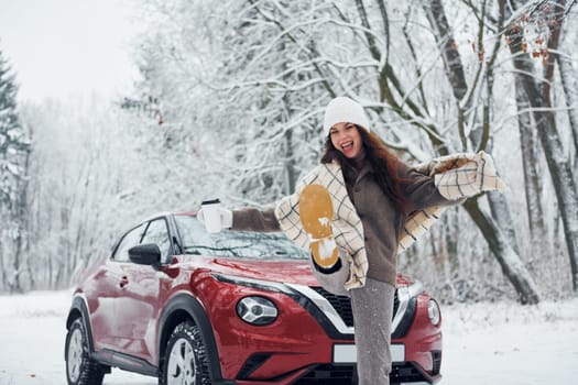 Beautiful winter background. Beautiful young woman is outdoors near her red automobile at winter time.