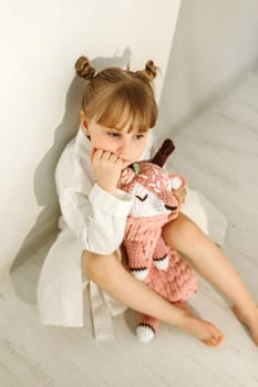 A girl in a dressing gown plays with a knitted deer.