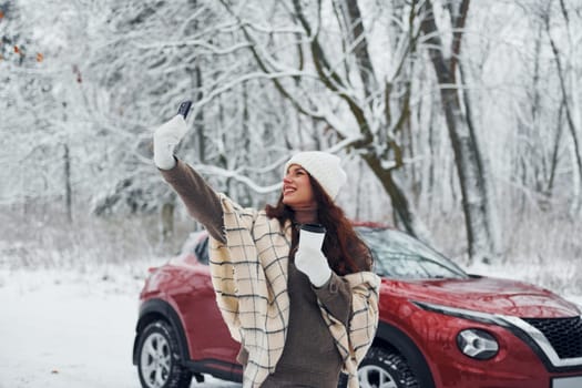 Beautiful nature. Young woman is outdoors near her red automobile at winter time.