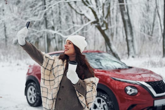 Beautiful nature. Young woman is outdoors near her red automobile at winter time.
