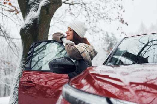 Walking out off car. Beautiful young woman is outdoors near her red automobile at winter time.