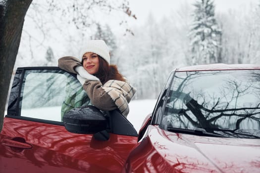 Walking out off car. Beautiful young woman is outdoors near her red automobile at winter time.
