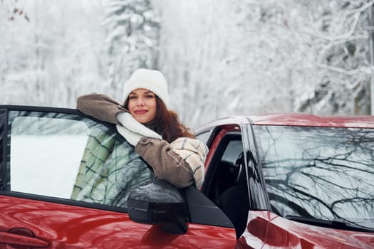Walking out off car. Beautiful young woman is outdoors near her red automobile at winter time.