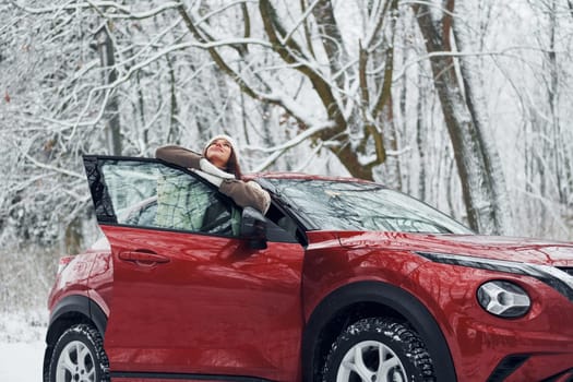 Walking out off car. Beautiful young woman is outdoors near her red automobile at winter time.