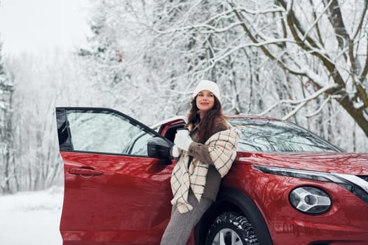 Walking out off car. Beautiful young woman is outdoors near her red automobile at winter time.