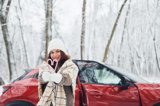 Non urban scene. Beautiful young woman is outdoors near her red automobile at winter time.
