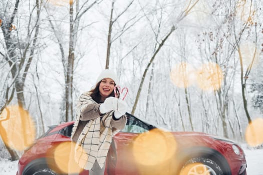 Non urban scene. Beautiful young woman is outdoors near her red automobile at winter time.