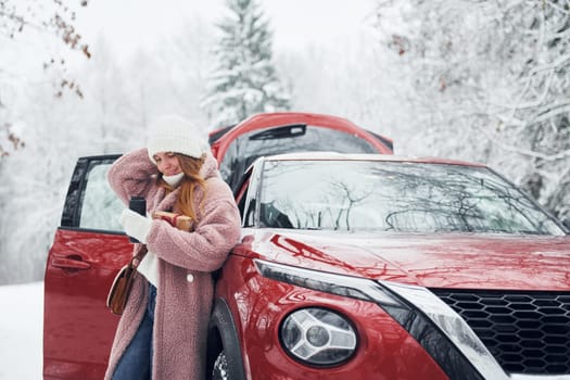 Having fun. Beautiful young woman is outdoors near her red automobile at winter time.