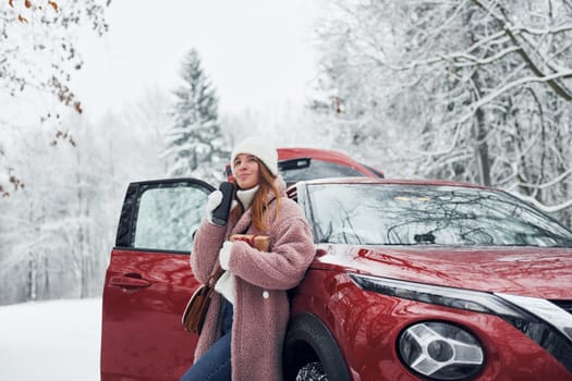 Having fun. Beautiful young woman is outdoors near her red automobile at winter time.