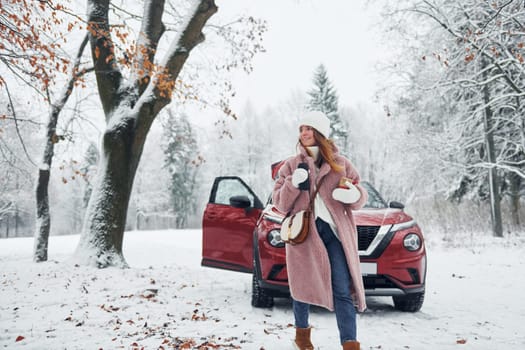 Having fun. Beautiful young woman is outdoors near her red automobile at winter time.