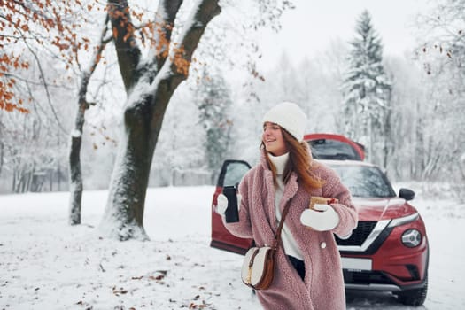 Having fun. Beautiful young woman is outdoors near her red automobile at winter time.