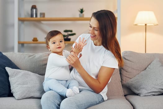 Sitting on the sofa. Mother with her little daughter is at home together.