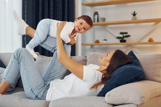 Playing on the sofa. Mother with her little daughter is at home together.