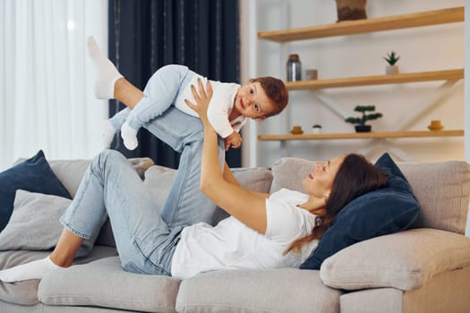 Playing on the sofa. Mother with her little daughter is at home together.