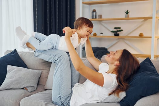 Playing on the sofa. Mother with her little daughter is at home together.