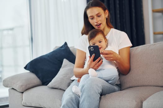 With smartphone in hand. Mother with her little daughter is at home together.