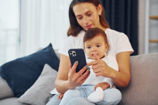 With smartphone in hand. Mother with her little daughter is at home together.