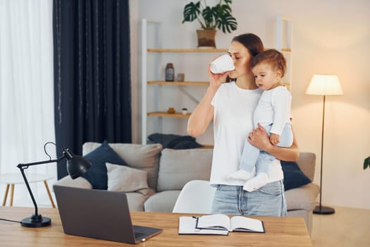 Using laptop. Mother with her little daughter is at home together.