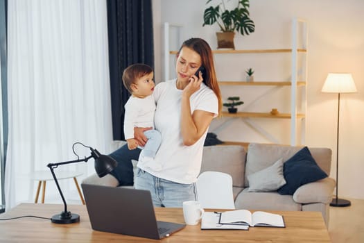 Laptop is on the table. Mother with her little daughter is at home together.